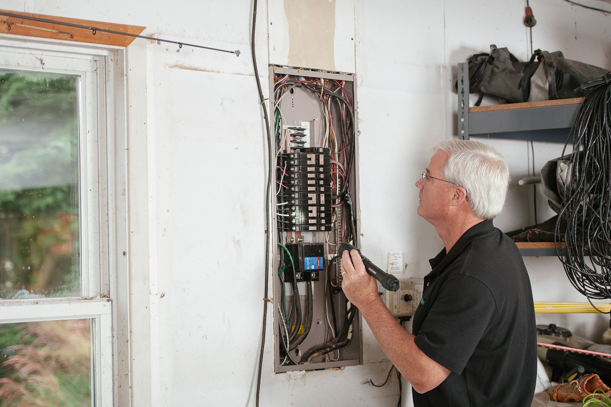 An electrician inspects a residential fuse box with a flashlight.
