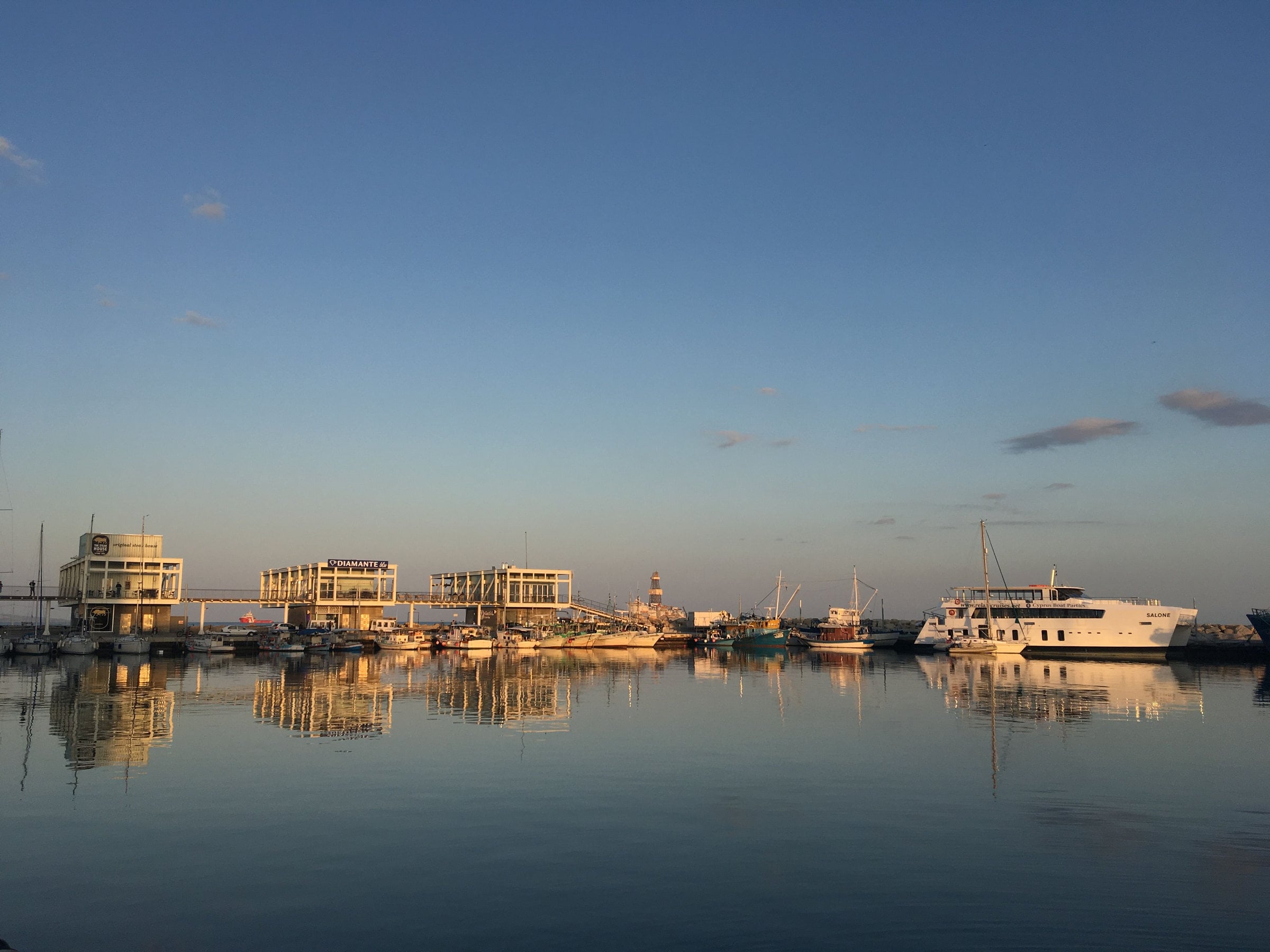 Evening view of Limassol Marina, Cyprus, with boats reflected in calm water.