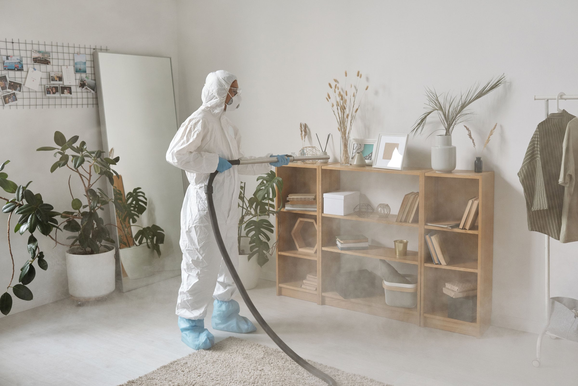 Technician in a protective suit fogging shelves in a bright modern living room.